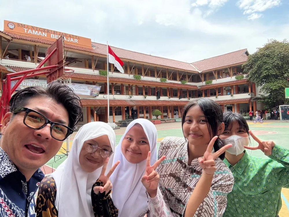 A participant taking a photograph with students in a Jakarta school courtyard